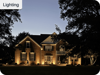 Landscape lighting illuminating the facade of a brick home at dusk