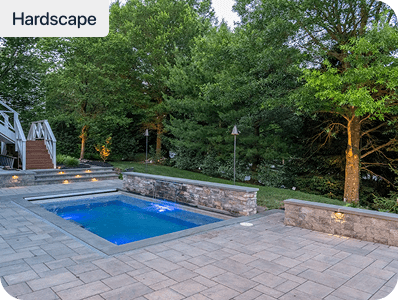 A small rectangular pool surrounded by stone pavers and low stone walls, with trees and greenery in the background. Steps lead up to a deck on the left. The scene is labeled Hardscape.