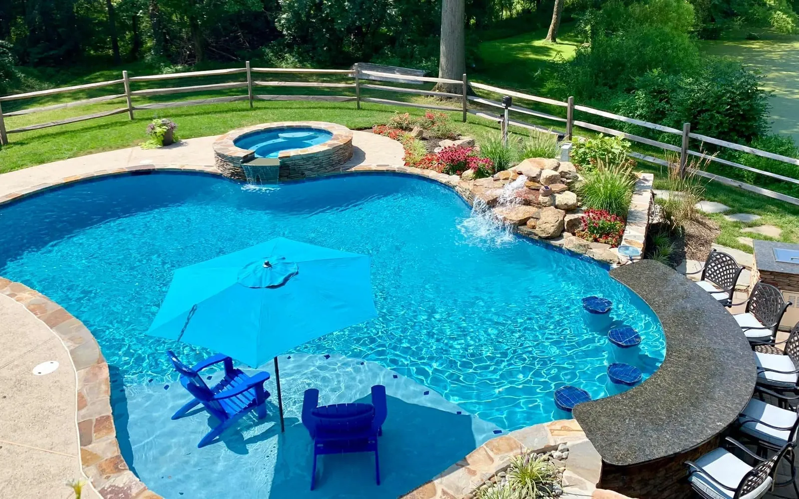 Phoenixville backyard pool with a stone edge, attached spa, waterfall, and swim-up bar by Blue Tree Outdoor Living
