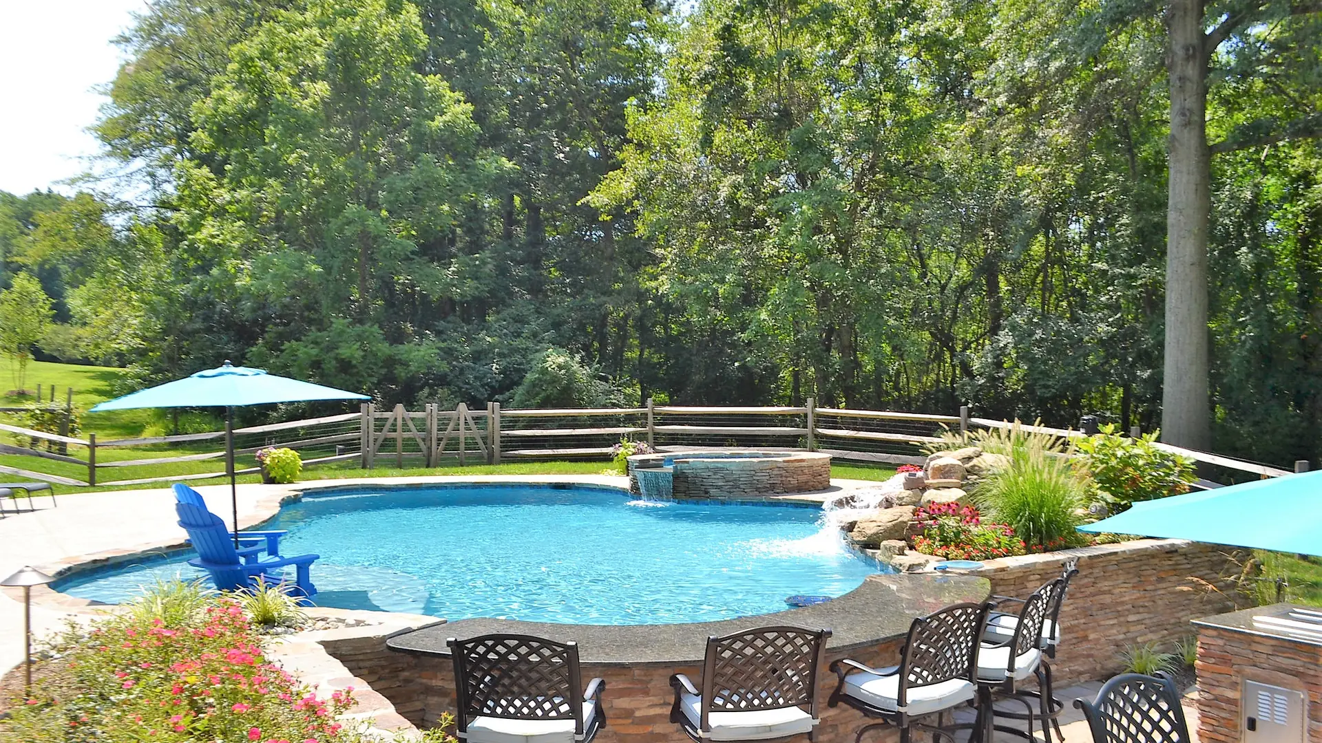 Completed backyard swimming pool with a raised spa, waterfall, poolside seating, and planted borders.