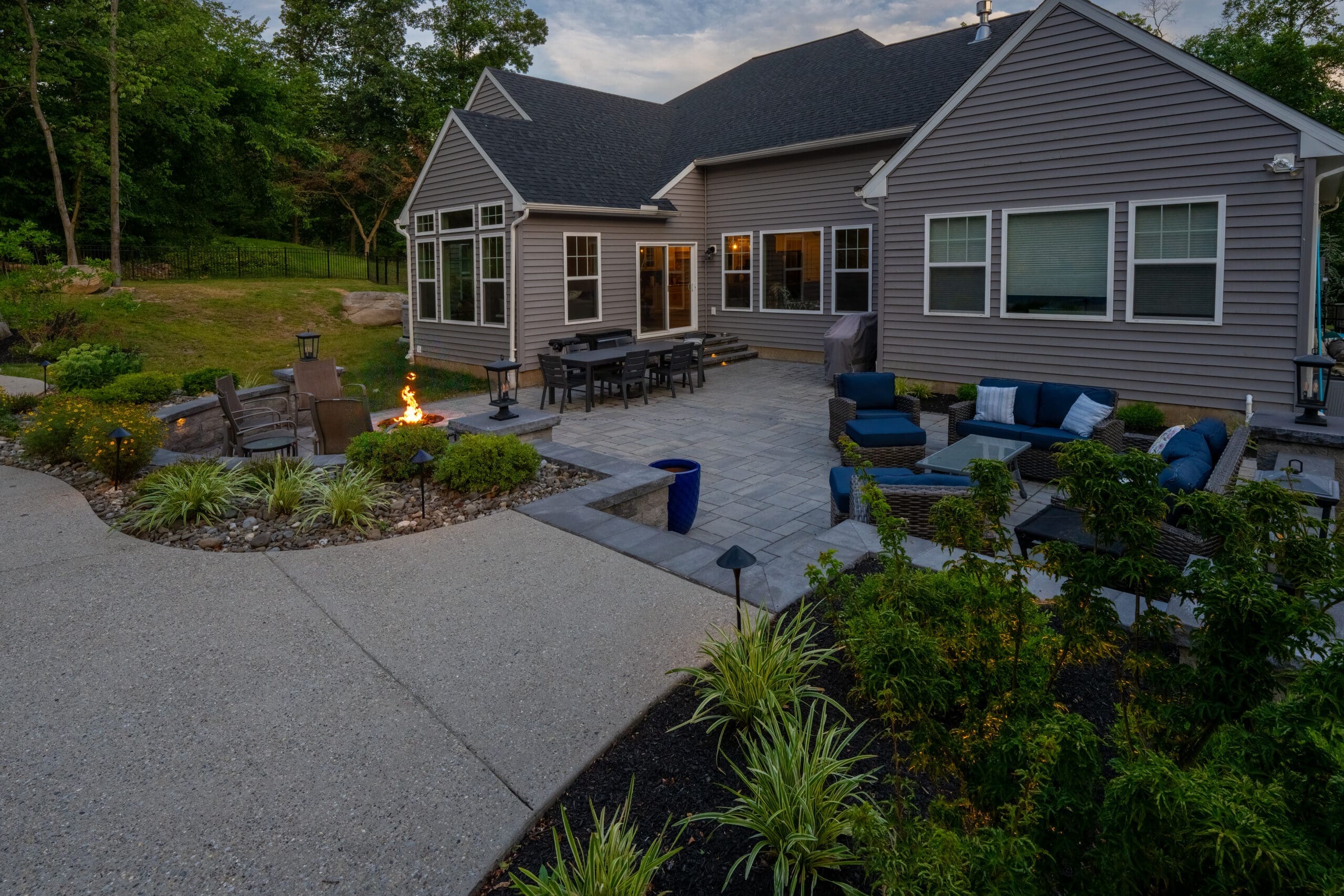A Pottstown backyard patio with a fire pit, outdoor dining table, blue seating, and landscaped garden beds.