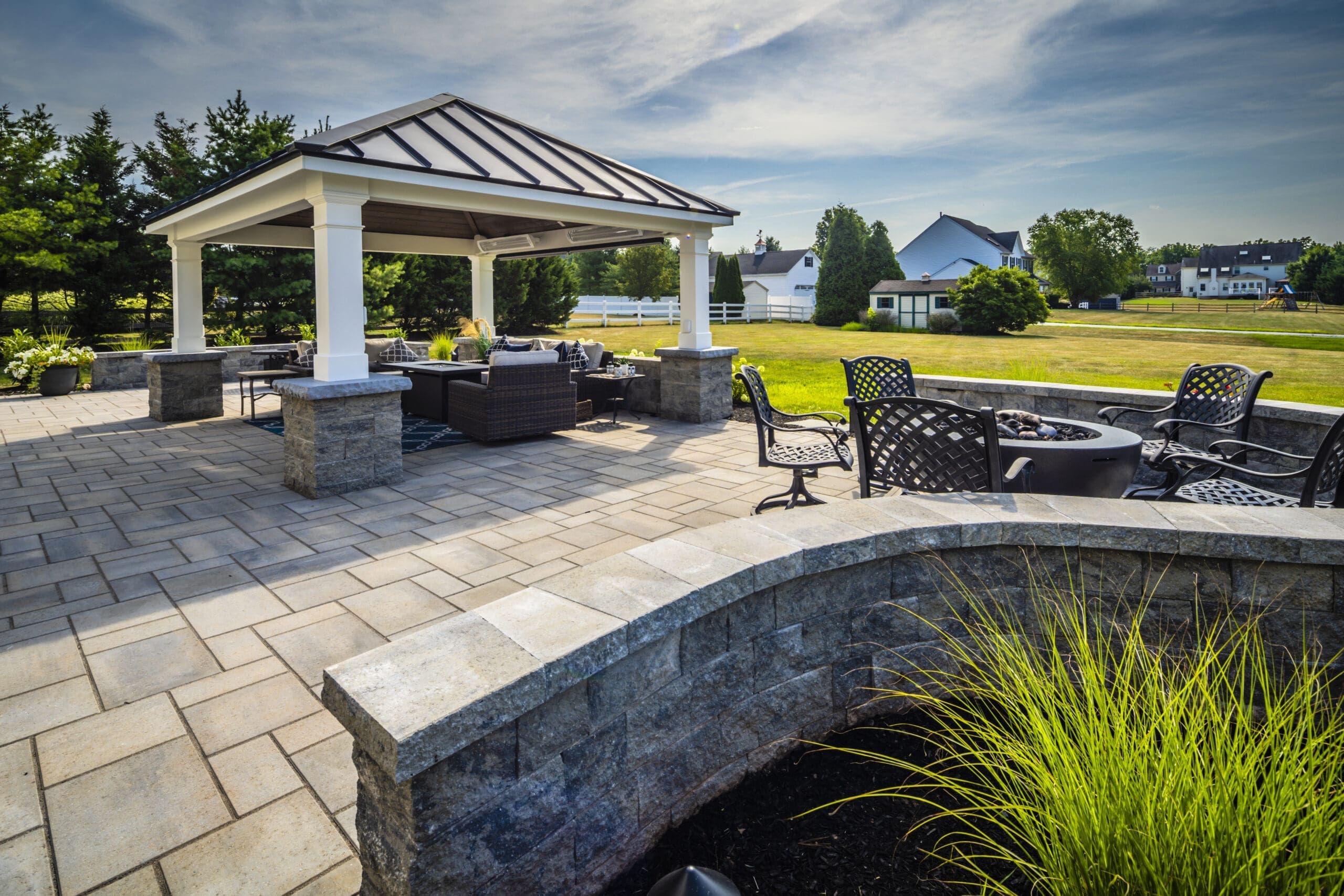 A spacious Skippack backyard patio with a covered seating area, stone pavers, a curved stone wall, and a fire pit.