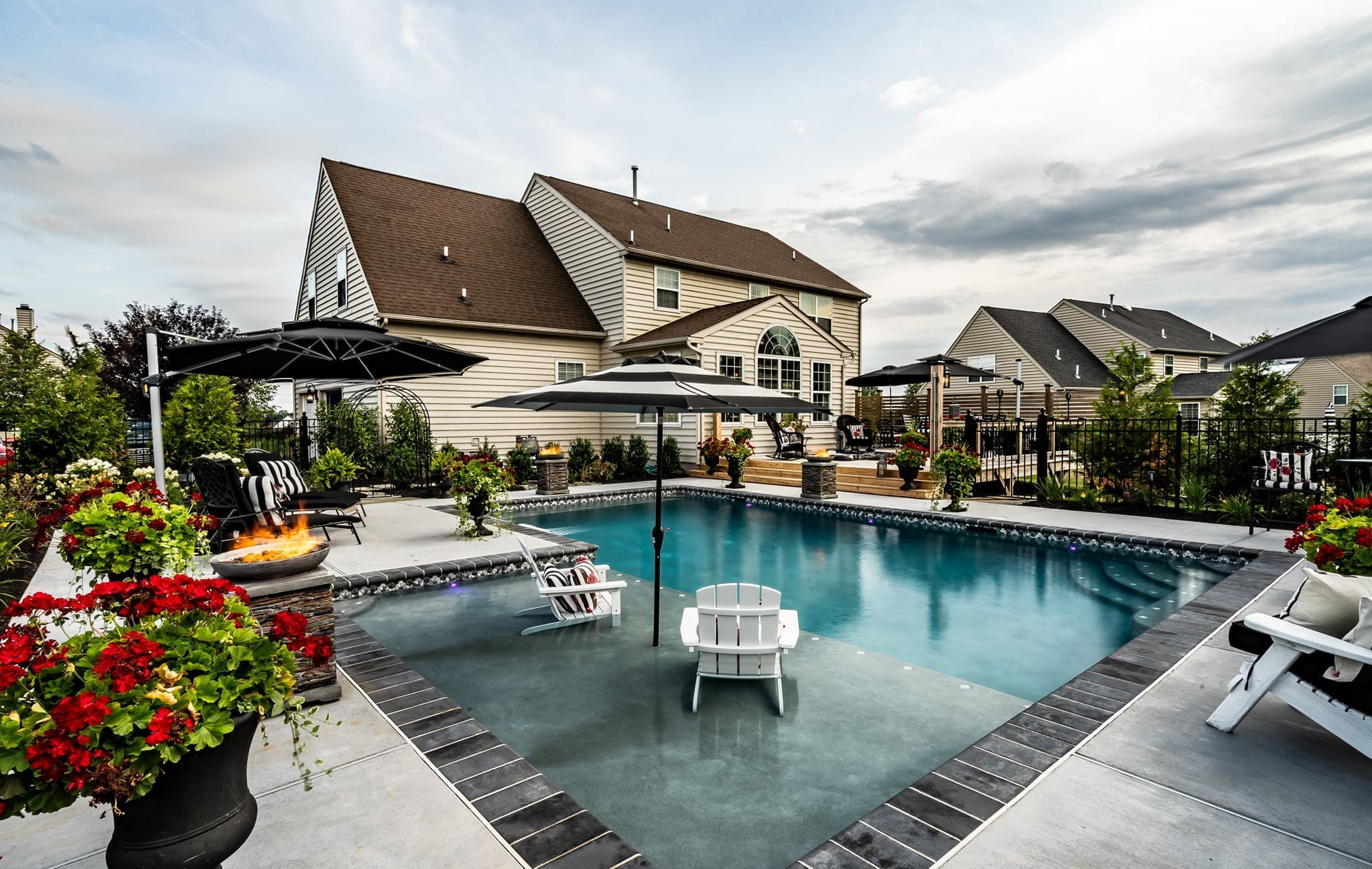 A modern Southeastern PA backyard pool with stone decking, lounge chairs, and lush landscaping.