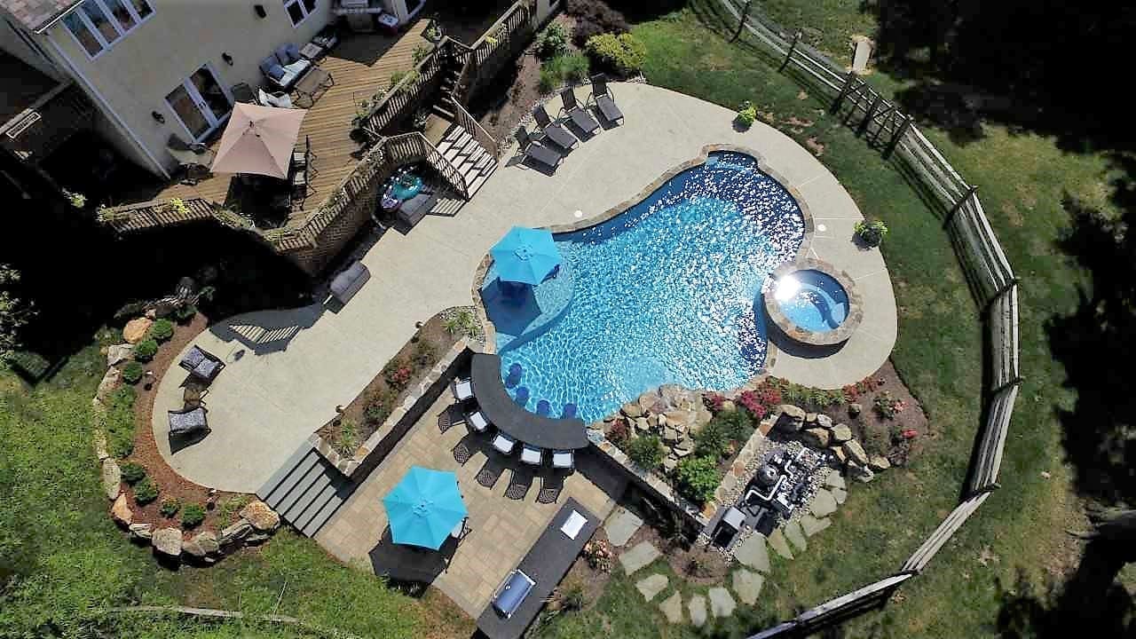 A Southeastern PA backyard with a custom pool, covered outdoor kitchen, dining area, fireplace, and landscaping.