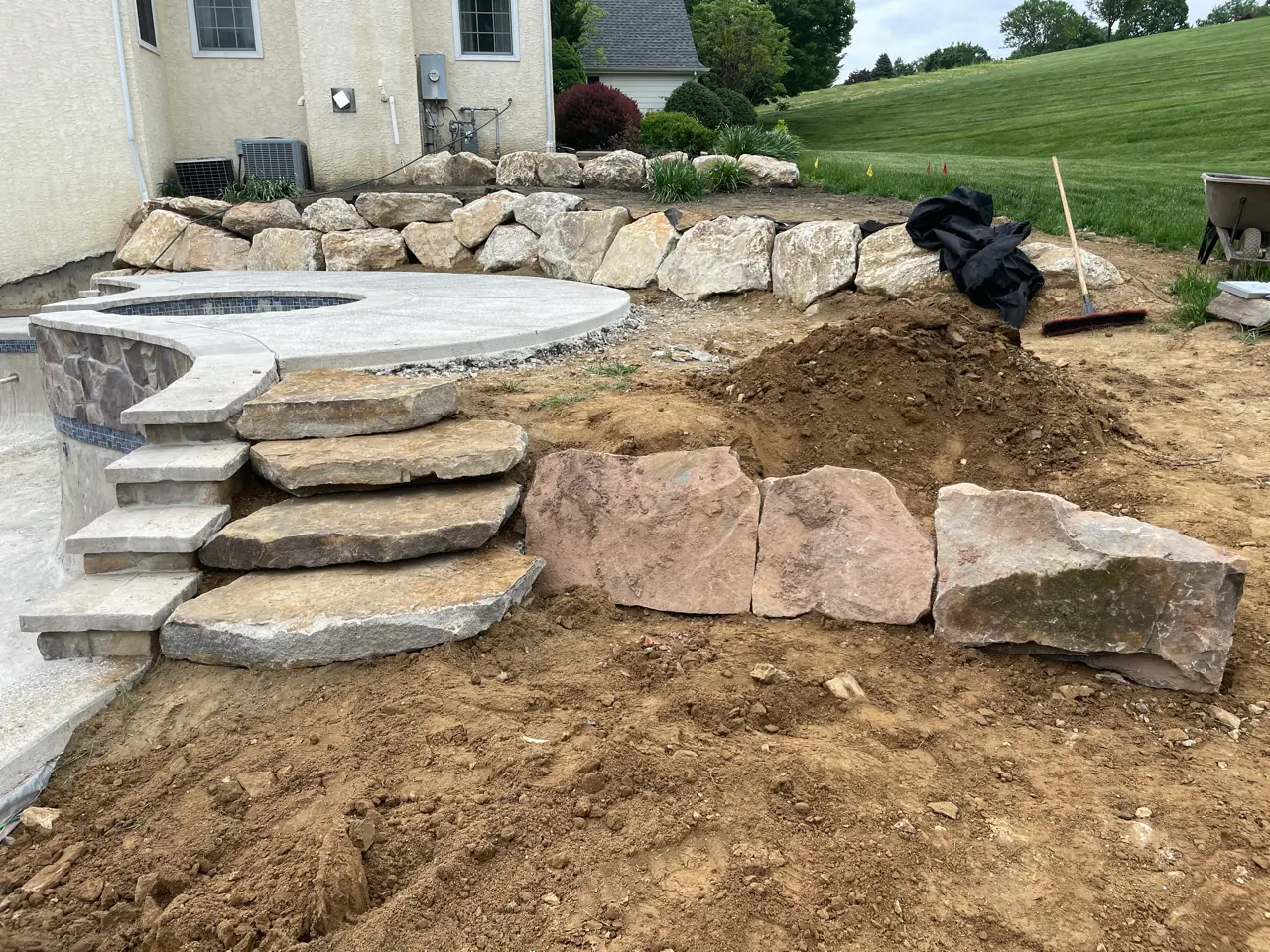 Natural boulder steps and raised spa during pool construction in West Chester, PA