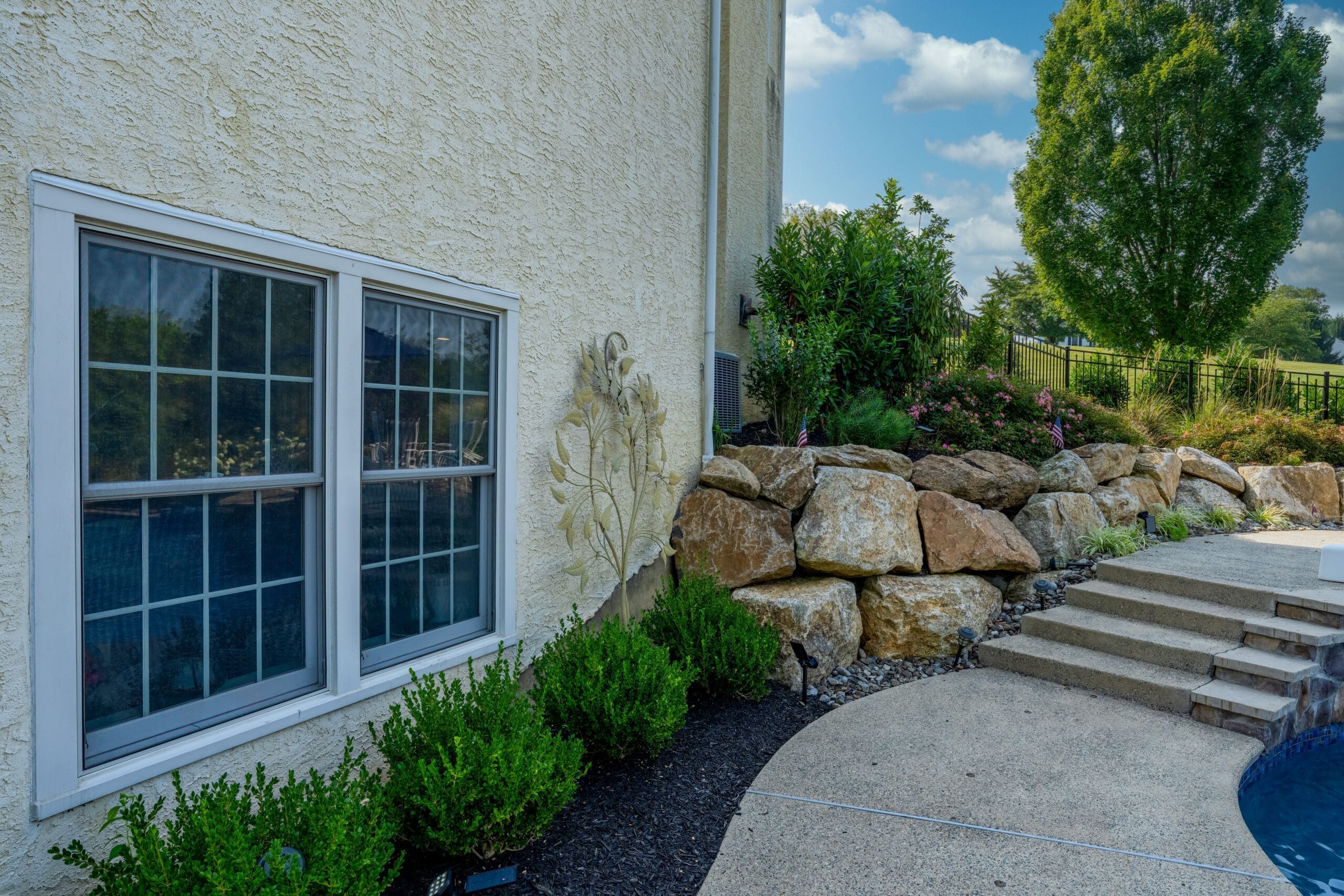 A West Chester backyard with stone stairs leading to a pool, large rocks, shrubs, and surrounding landscaping.