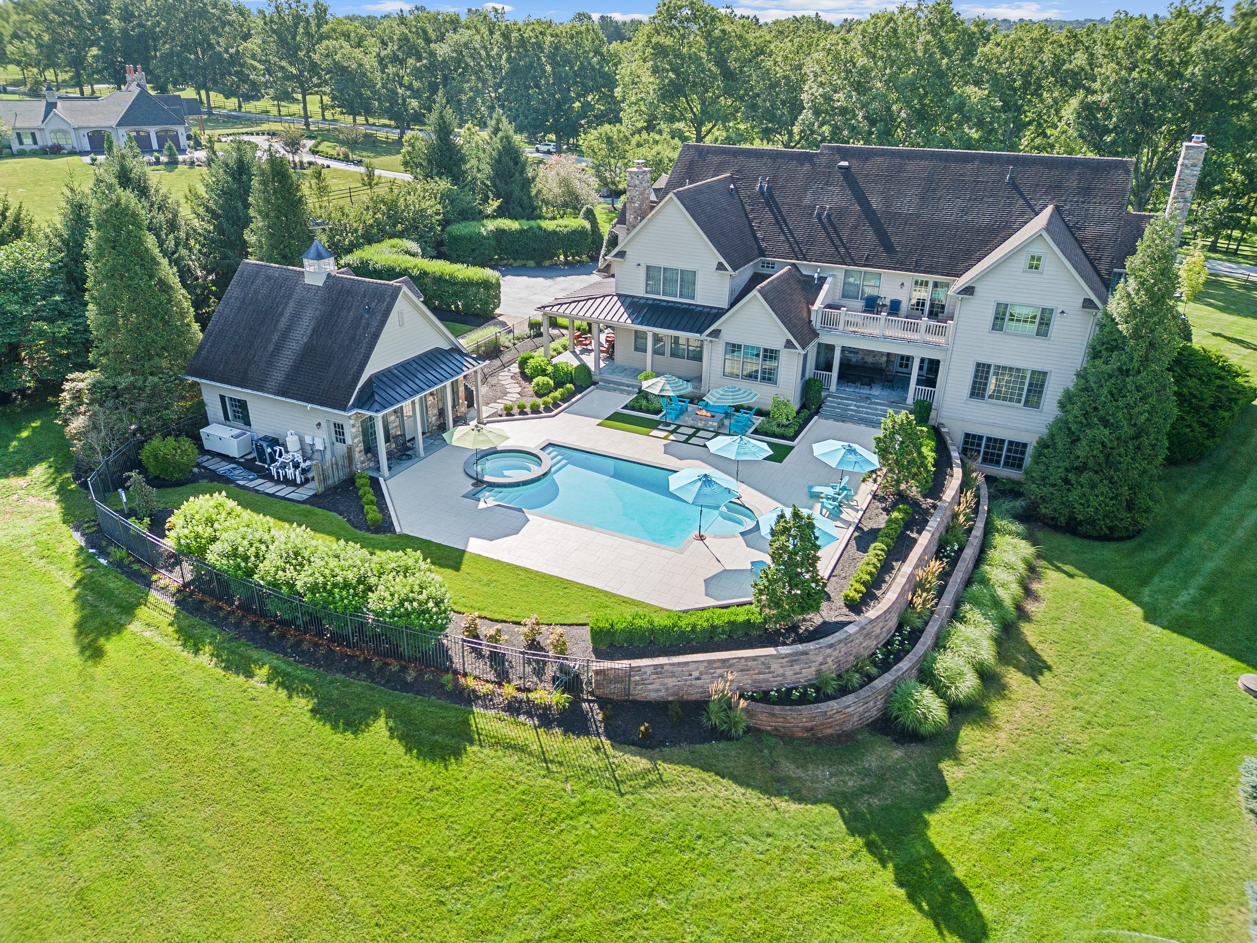 Aerial view of a completed custom pool and spa with a paver patio, landscaped beds, and curved retaining walls by Blue Tree Outdoor Living.